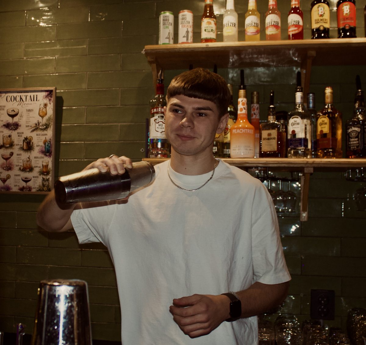 A bartender shaking a cocktail in front of the back bar